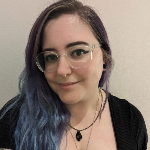 Beki Strauser | Web Developer | A white skinned feminine person with long blue hair, glasses, a nose ring, and multiple necklaces. They're wearing a black shirt, and they are smiling.