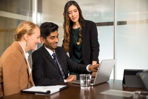 Female and Male sitting and one female standing and looking into a laptop