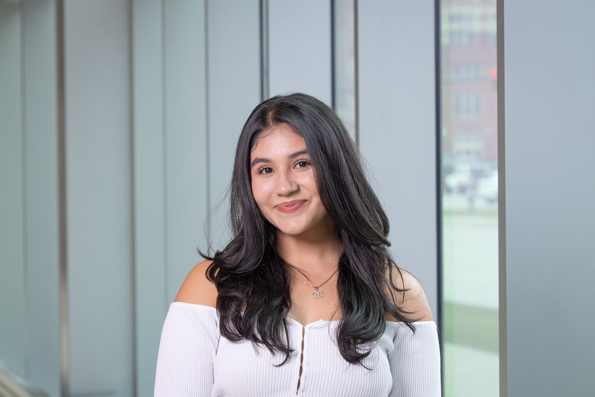 Fabiola Fraire Martinez wears a white, off-the-shoulder blouse, long dark hair, and smiling.