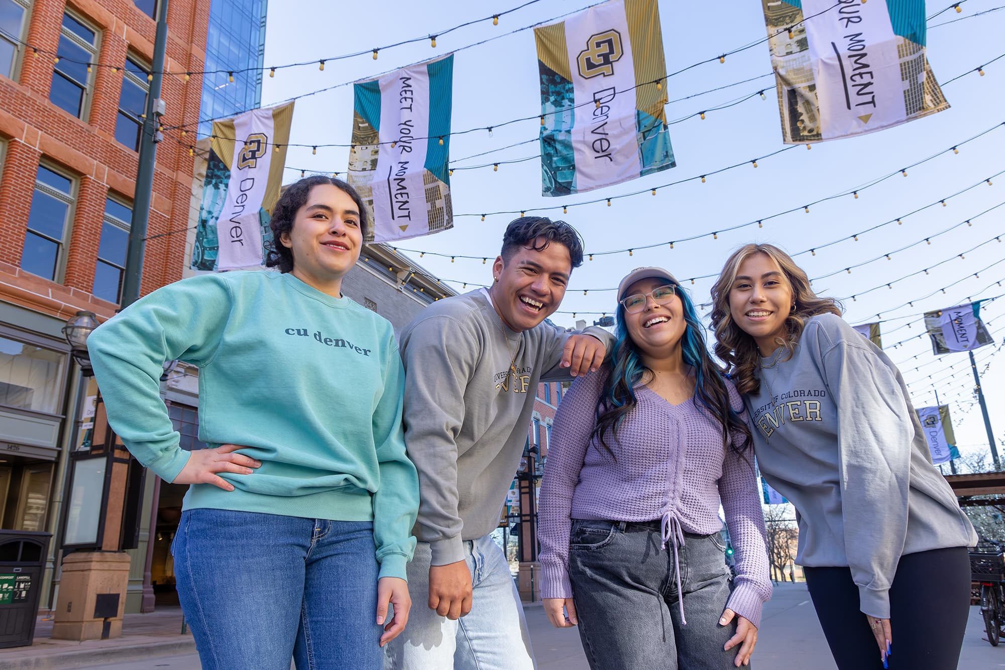 Four students dressed in CU Denver gear smiling in Larimer square.