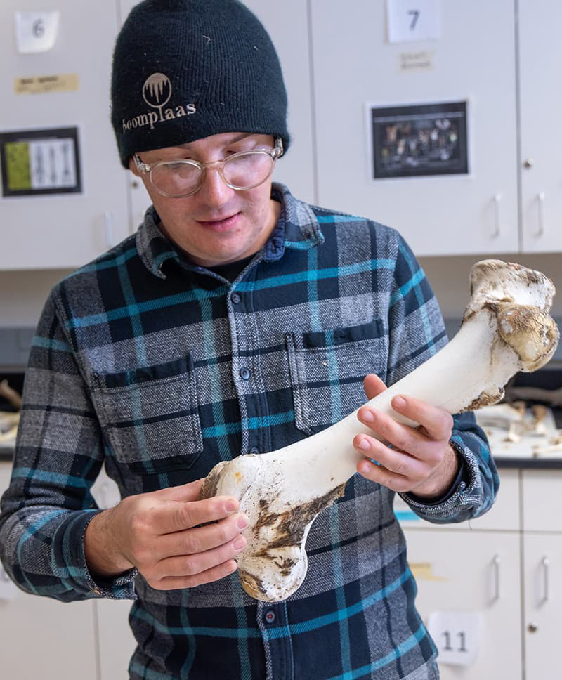 Man in a blue plaid flannel holding a large bone.