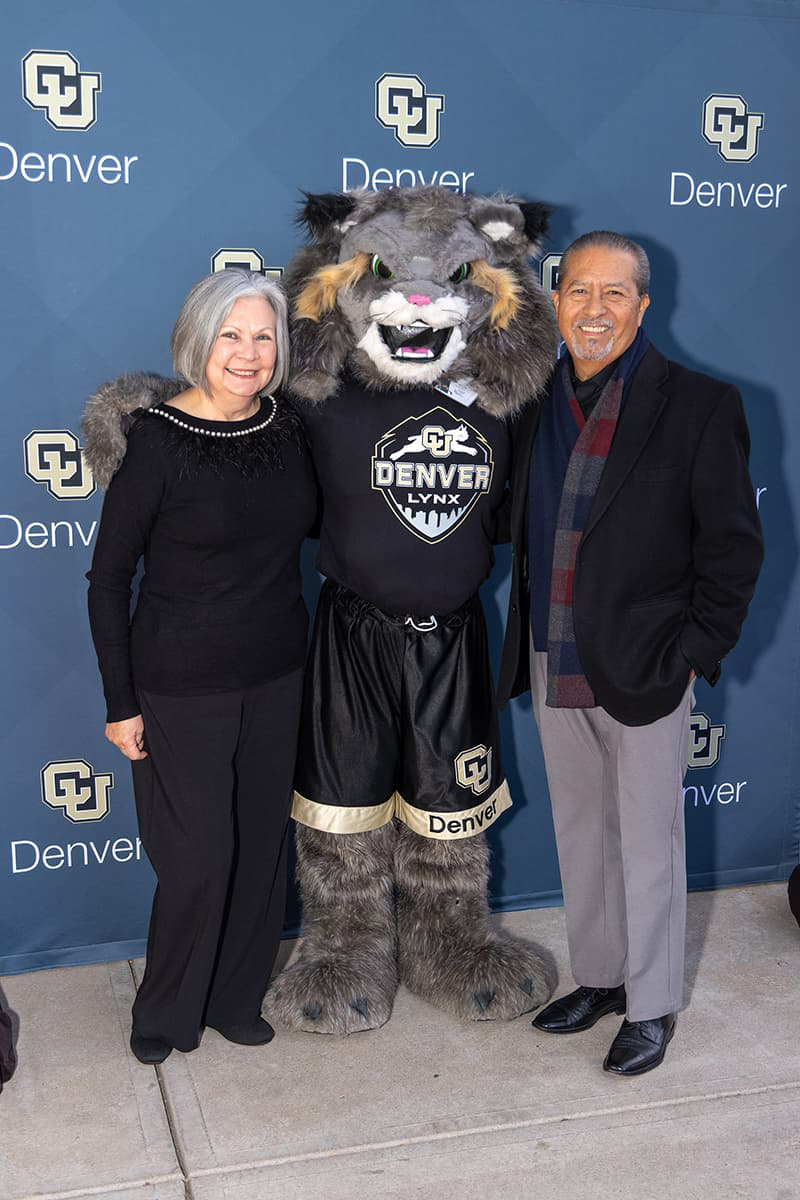 Two donors and Milo the Lynx mascot stand in front of a CU Denver backdrop.