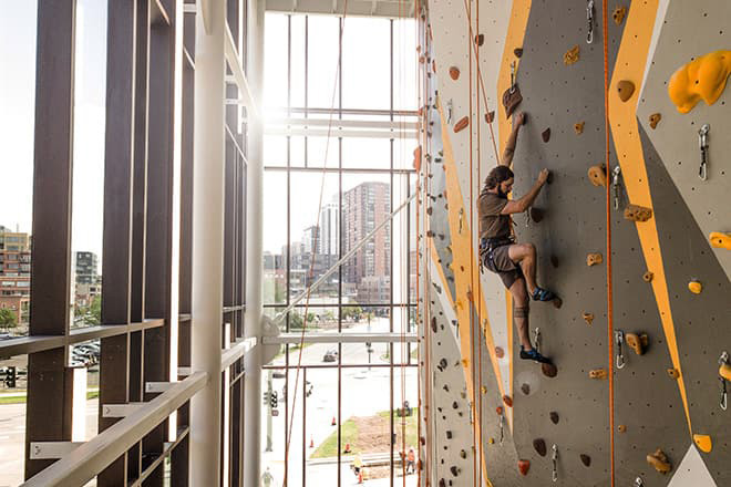 Man half way up the 38 foot rock climbing wall in the Lola & Rob Salazar Student Wellness Center.