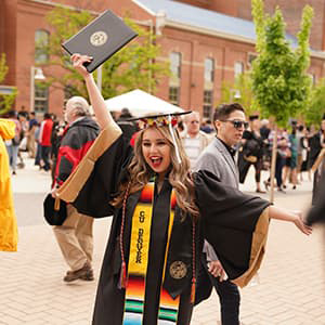 CU Denver Graduate celebrating with raised arms and an open-mouth smile
