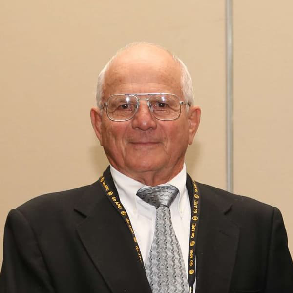 Al Ruckman wearing a suite and tie with silver-rimmed glasses, and short white hair, smiling.