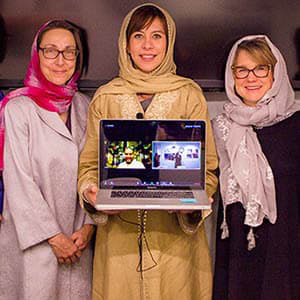 Alaa Al-Ban with two women hold a computer with her final project