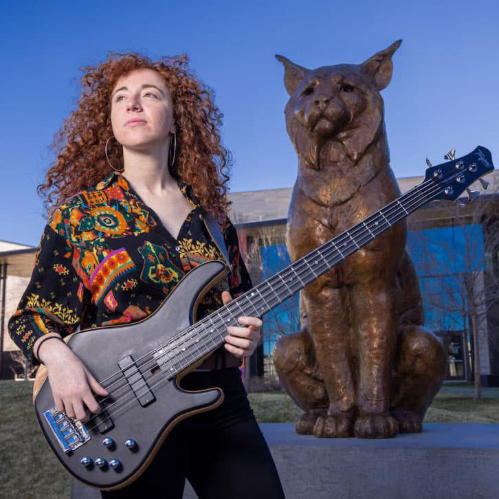 Zoe Moff holding a guitar standing in front of the bronze Lynx.