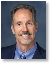 Smiling Caucasian Male with gray hair and beard wearing a blue jacket, shirt and tie. 