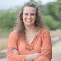 Headshot of Becca Gaffney outdoors in business casual blouse with arms folded smiling