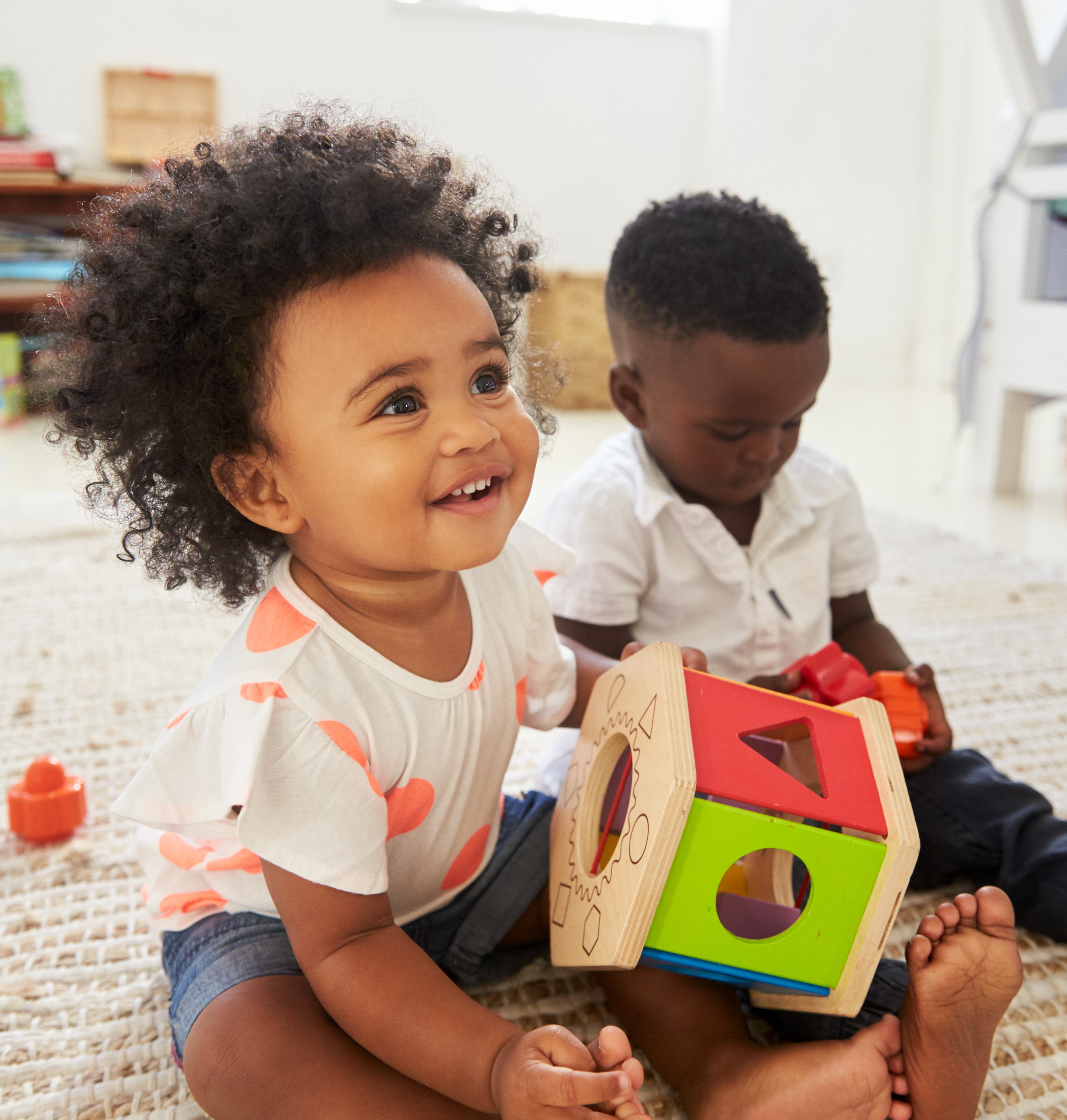 Young girl and boy sitting on floor, playing with shape sorting toys.