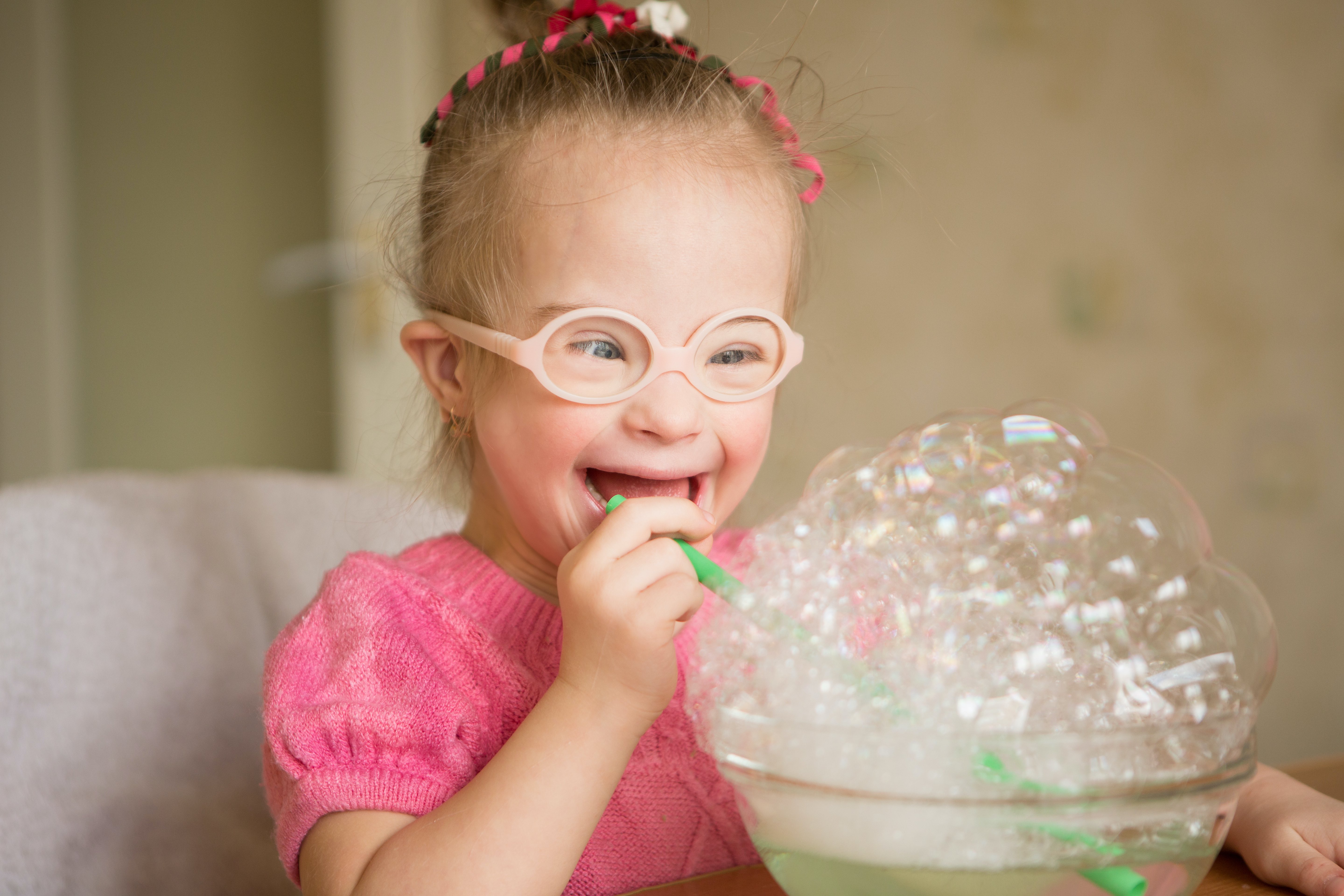 Little girl with disability smiling and blowing bubbles.