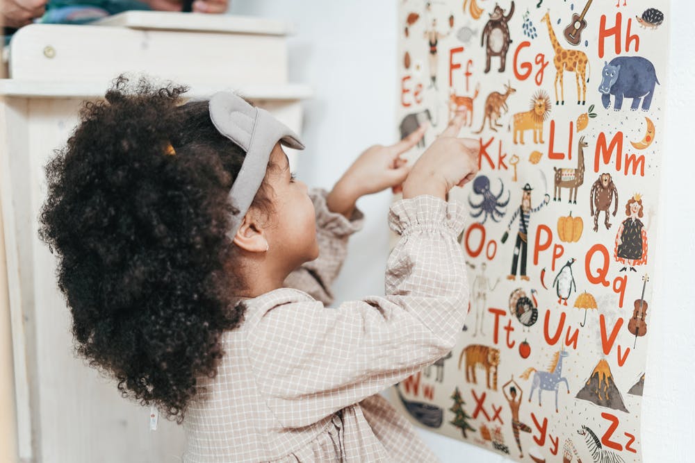 A young girl points at colorful pictures on a poster