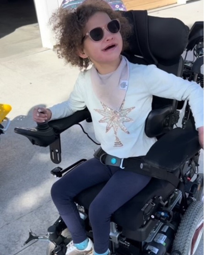 Jordy smiles, hand on the joystick of her power wheelchair