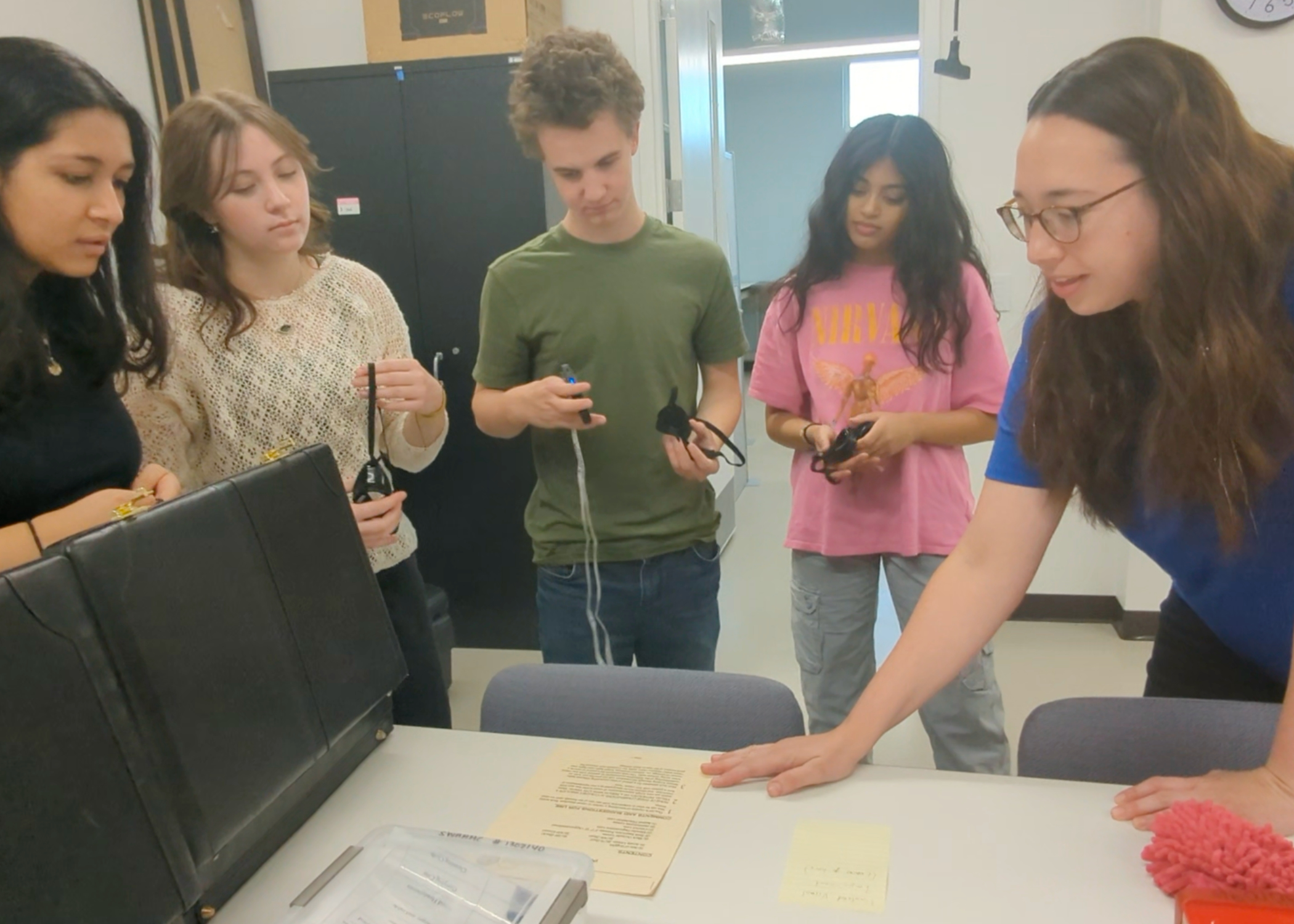 A group of teenagers with an instructor holding various devices and reading instructions